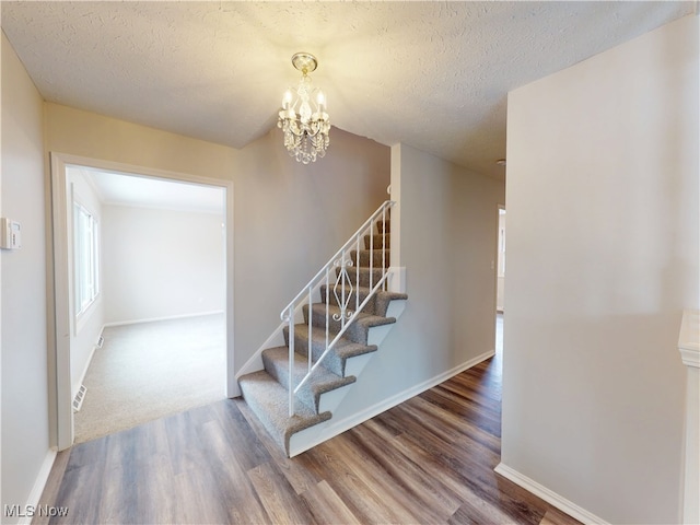 stairway with wood-type flooring, a chandelier, and a textured ceiling