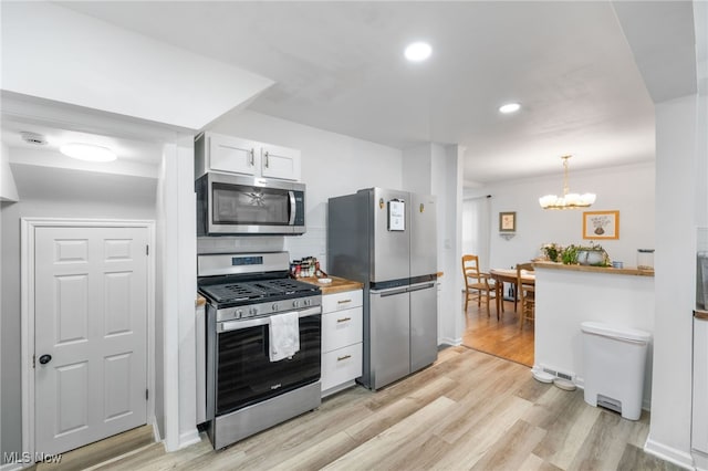 kitchen featuring white cabinetry, decorative light fixtures, stainless steel appliances, and light wood-type flooring