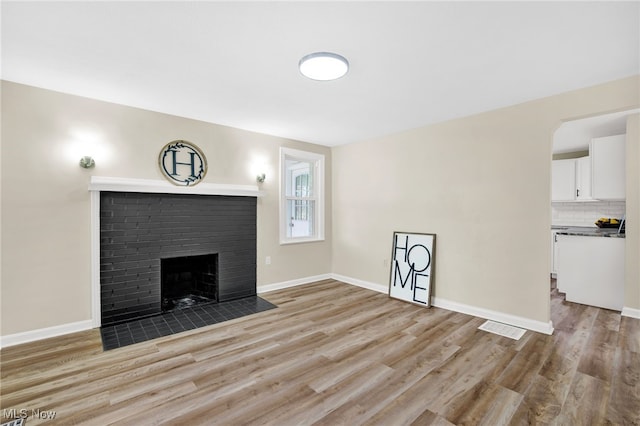 unfurnished living room with a brick fireplace and light hardwood / wood-style flooring