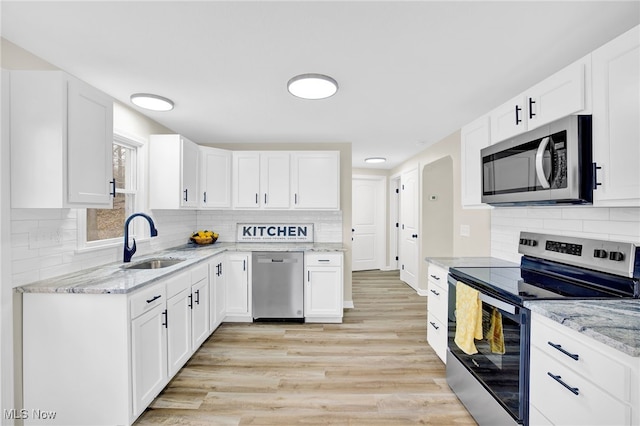 kitchen with tasteful backsplash, sink, white cabinets, stainless steel appliances, and light wood-type flooring