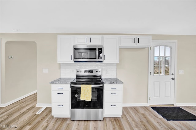 kitchen with appliances with stainless steel finishes, tasteful backsplash, white cabinets, light stone countertops, and light wood-type flooring