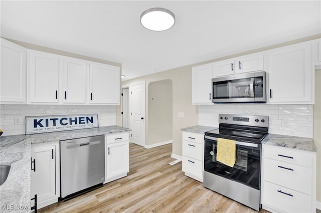 kitchen with stainless steel appliances, light stone countertops, white cabinets, and light hardwood / wood-style floors