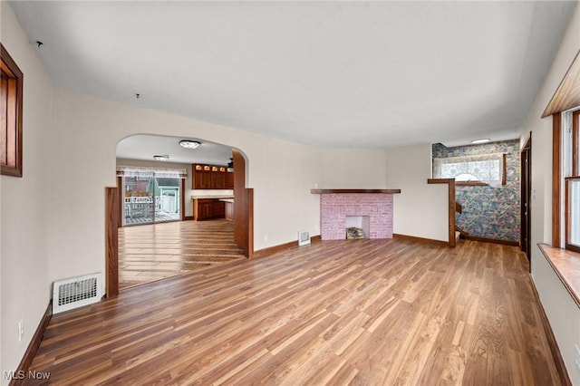 unfurnished living room featuring wood-type flooring and a brick fireplace