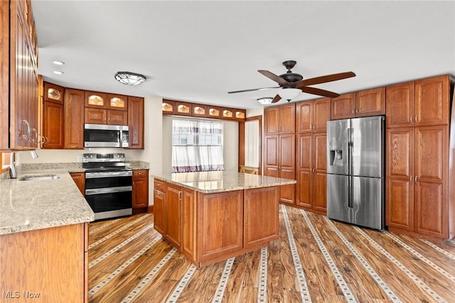 kitchen featuring sink, a center island, hardwood / wood-style flooring, stainless steel appliances, and light stone countertops