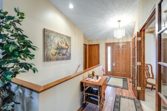 foyer featuring lofted ceiling, a chandelier, a textured ceiling, and light wood-type flooring