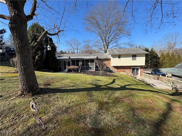 rear view of house featuring brick siding, fence, a sunroom, stairs, and a lawn