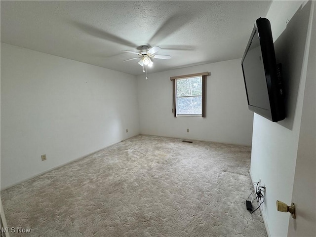 carpeted empty room with visible vents, ceiling fan, and a textured ceiling