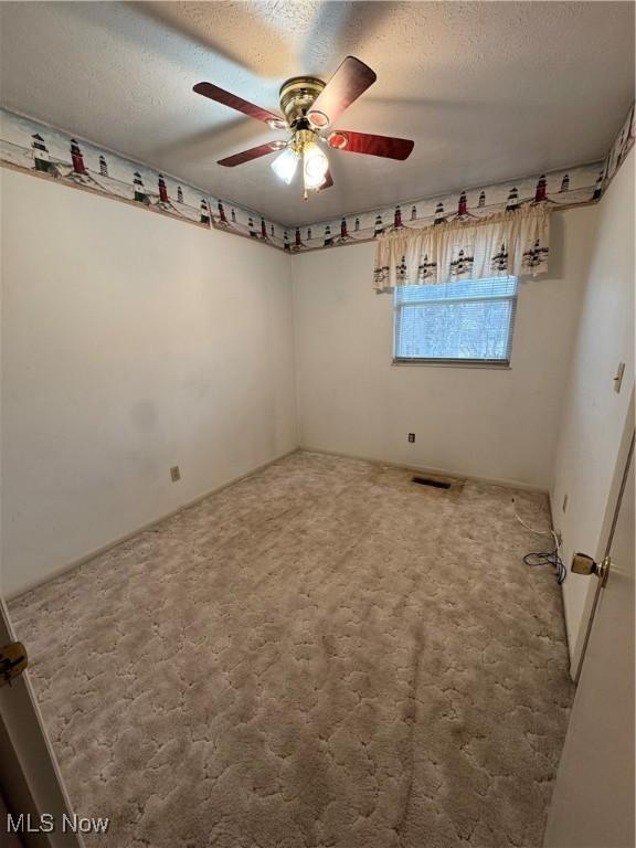 carpeted spare room with a textured ceiling, ceiling fan, and visible vents