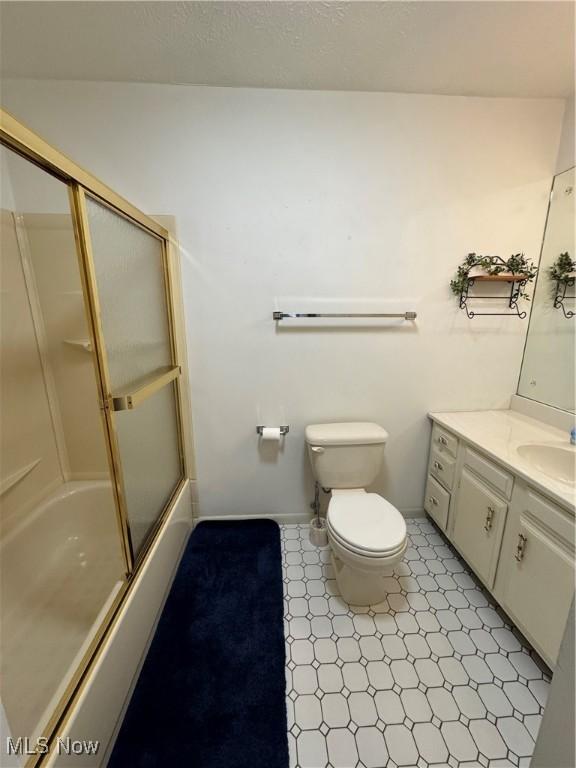 full bath with a textured ceiling, toilet, shower / bath combination with glass door, vanity, and baseboards