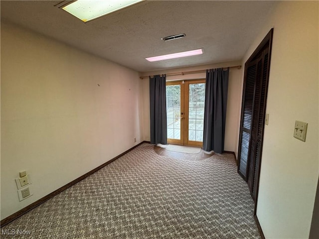 spare room with carpet, french doors, visible vents, a textured ceiling, and baseboards