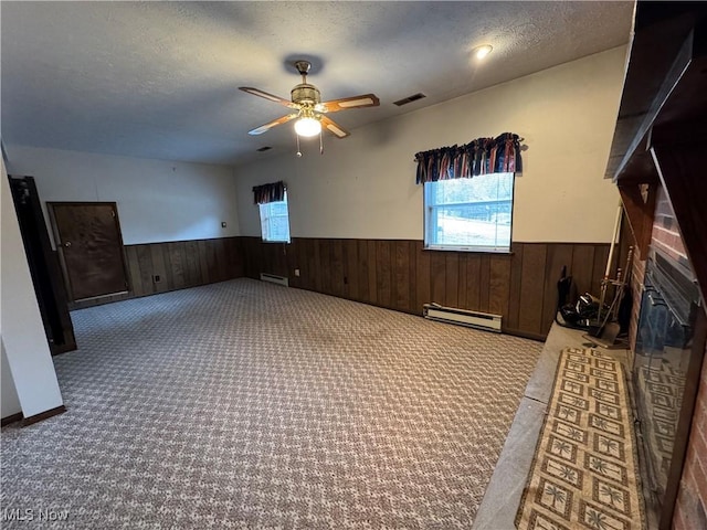 empty room featuring a baseboard heating unit, a glass covered fireplace, wainscoting, and a textured ceiling