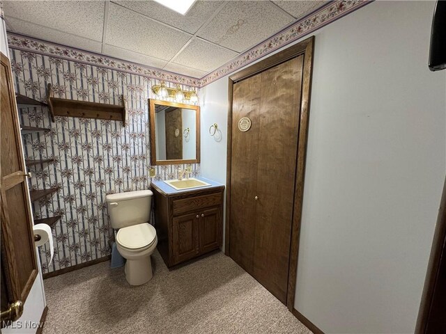 bathroom with a paneled ceiling, toilet, vanity, baseboards, and wallpapered walls