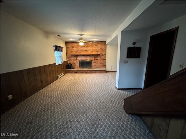 unfurnished living room with a wainscoted wall, a fireplace, a baseboard radiator, a ceiling fan, and a textured ceiling