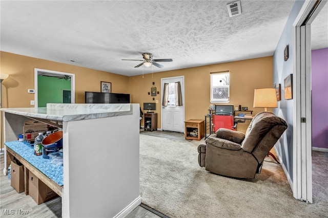 living room featuring ceiling fan, light colored carpet, and a textured ceiling