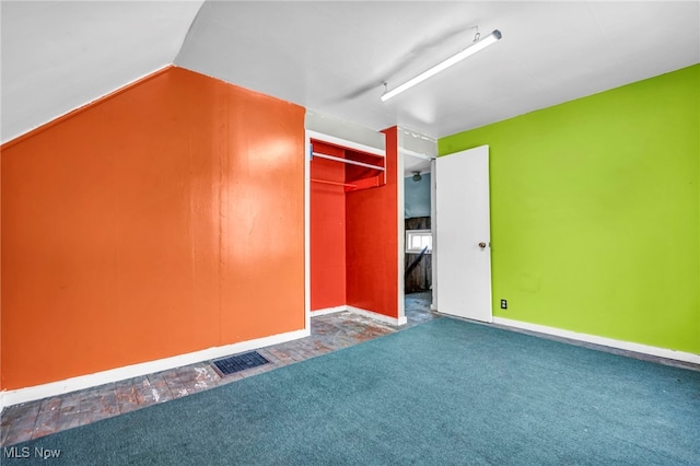 unfurnished bedroom featuring lofted ceiling, a closet, and dark colored carpet