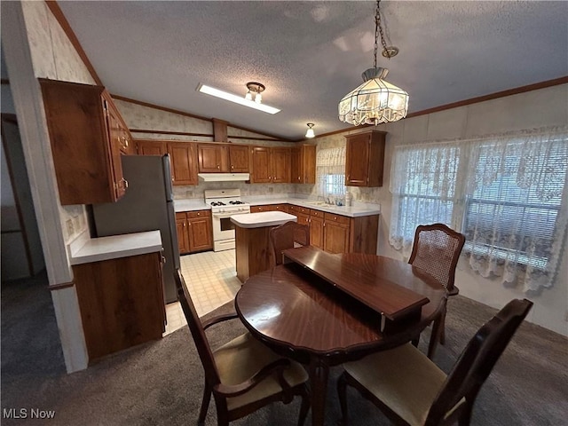 kitchen featuring lofted ceiling, gas range gas stove, hanging light fixtures, a textured ceiling, and stainless steel fridge