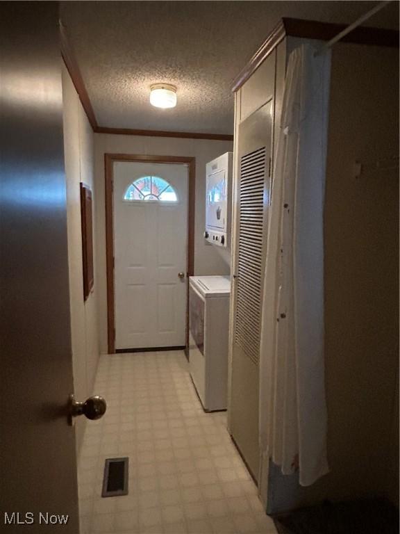 doorway with stacked washer and dryer, ornamental molding, and a textured ceiling