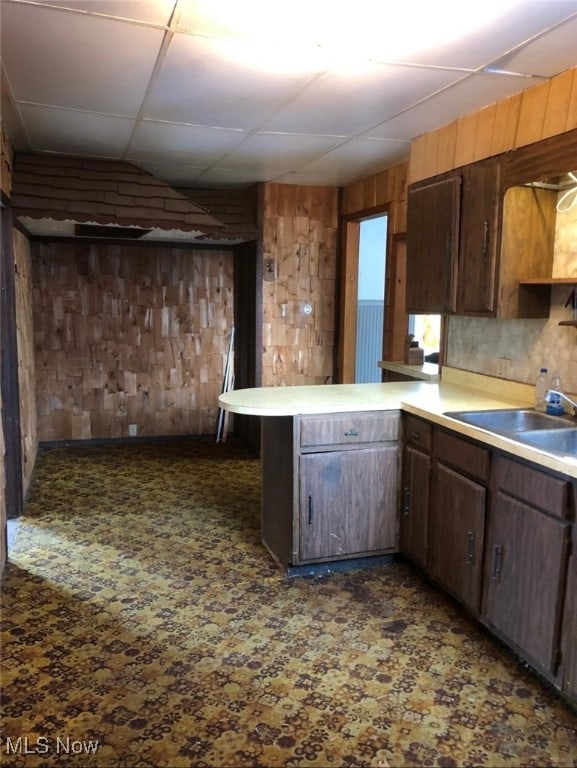 kitchen with sink, dark brown cabinets, kitchen peninsula, and wood walls