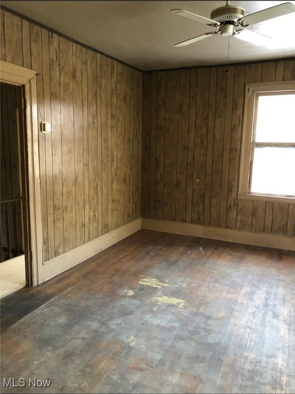 spare room featuring dark wood-type flooring, ceiling fan, and wood walls