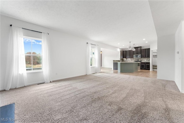 unfurnished living room with a textured ceiling, light carpet, and a wealth of natural light