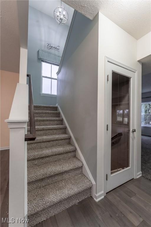 stairway featuring a wealth of natural light, wood-type flooring, and a chandelier