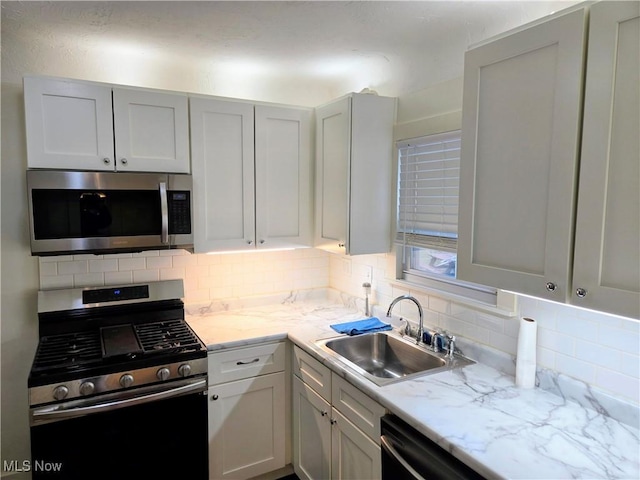 kitchen with sink, white cabinetry, stainless steel appliances, tasteful backsplash, and light stone counters