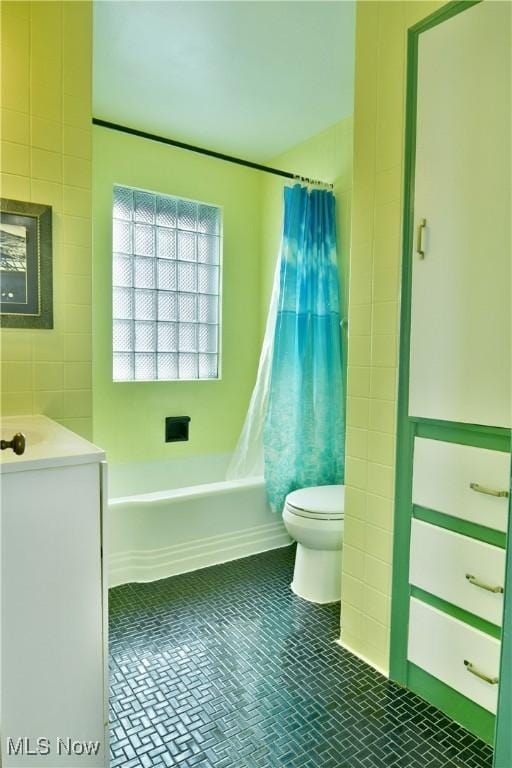 full bathroom with shower / tub combo with curtain, tile patterned floors, toilet, tile walls, and vanity