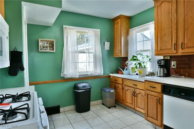 kitchen featuring white gas range, dishwashing machine, decorative backsplash, and light tile patterned floors