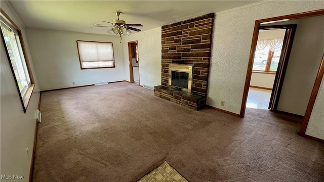 unfurnished living room with crown molding, carpet, a stone fireplace, and ceiling fan