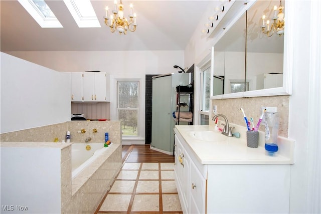 bathroom featuring tiled tub, lofted ceiling with skylight, a notable chandelier, and vanity