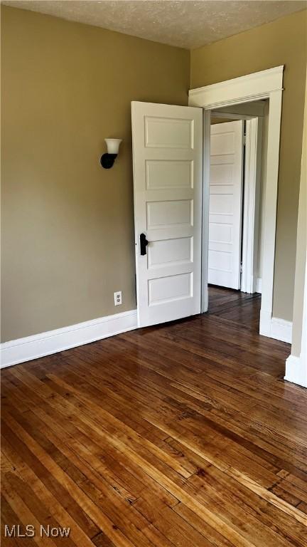 empty room with dark wood-type flooring and a textured ceiling