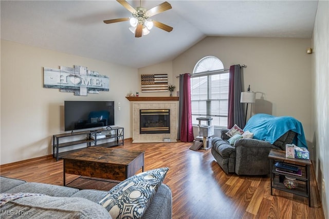 living room featuring a tiled fireplace, hardwood / wood-style floors, vaulted ceiling, and ceiling fan