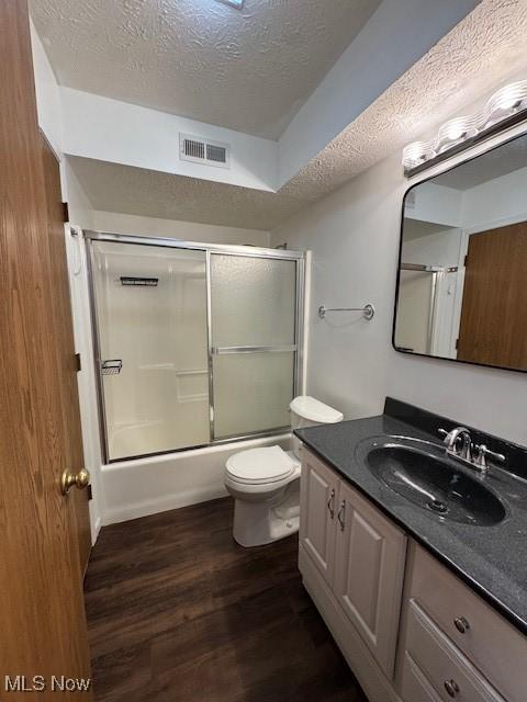 full bathroom featuring enclosed tub / shower combo, hardwood / wood-style floors, vanity, a textured ceiling, and toilet