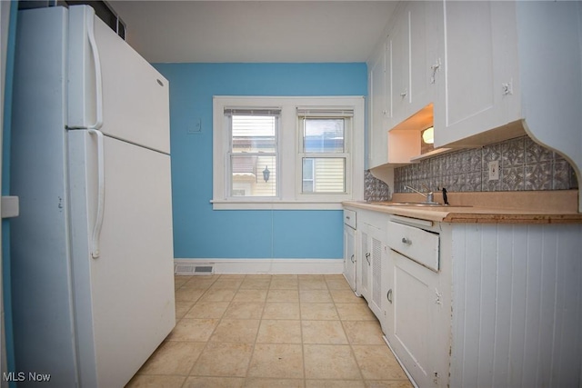 kitchen with tasteful backsplash, sink, white cabinets, white refrigerator, and light tile patterned floors