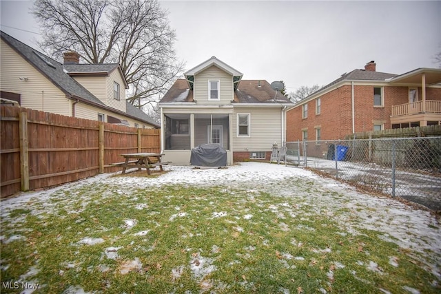 snow covered rear of property featuring a sunroom and a yard