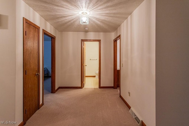 hallway featuring light colored carpet and a textured ceiling