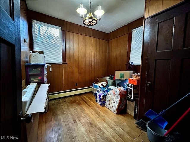 interior space featuring an inviting chandelier, wood walls, light wood-type flooring, and a baseboard heating unit