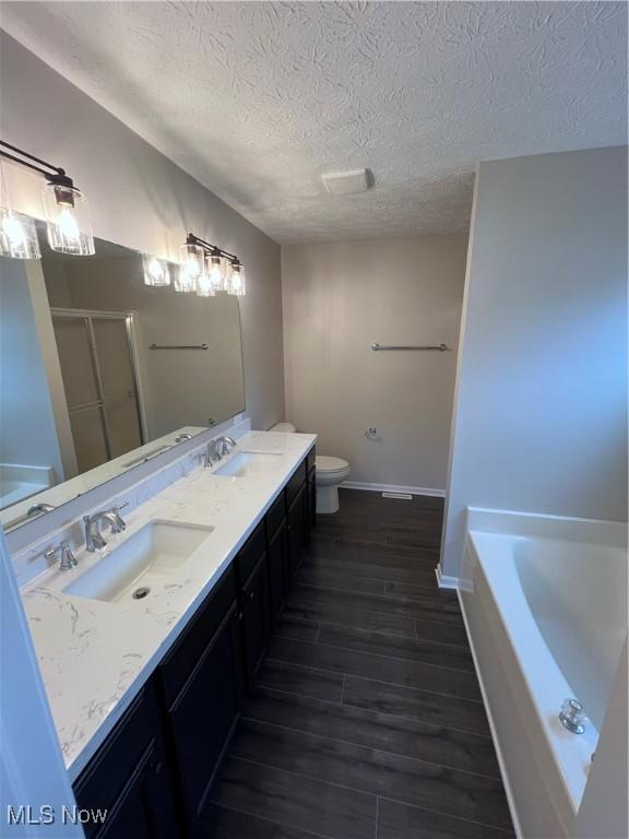 full bathroom featuring shower with separate bathtub, hardwood / wood-style flooring, vanity, toilet, and a textured ceiling