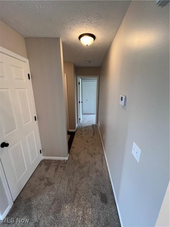 hallway featuring a textured ceiling and dark colored carpet