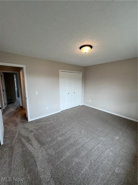 unfurnished bedroom with a closet, a textured ceiling, and dark colored carpet