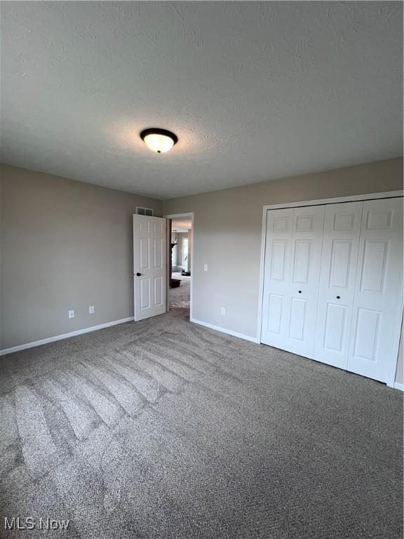 unfurnished bedroom featuring carpet flooring, a textured ceiling, and a closet