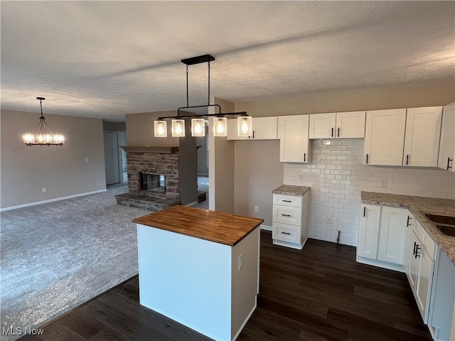 kitchen with dark wood-type flooring, light stone counters, a center island, pendant lighting, and white cabinets