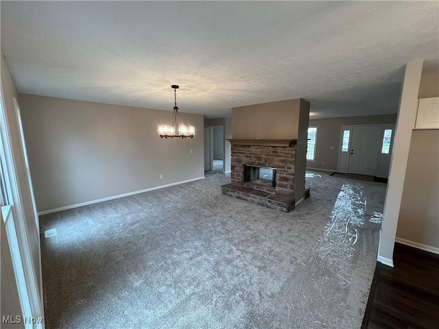 unfurnished living room with dark colored carpet, a textured ceiling, a fireplace, and an inviting chandelier