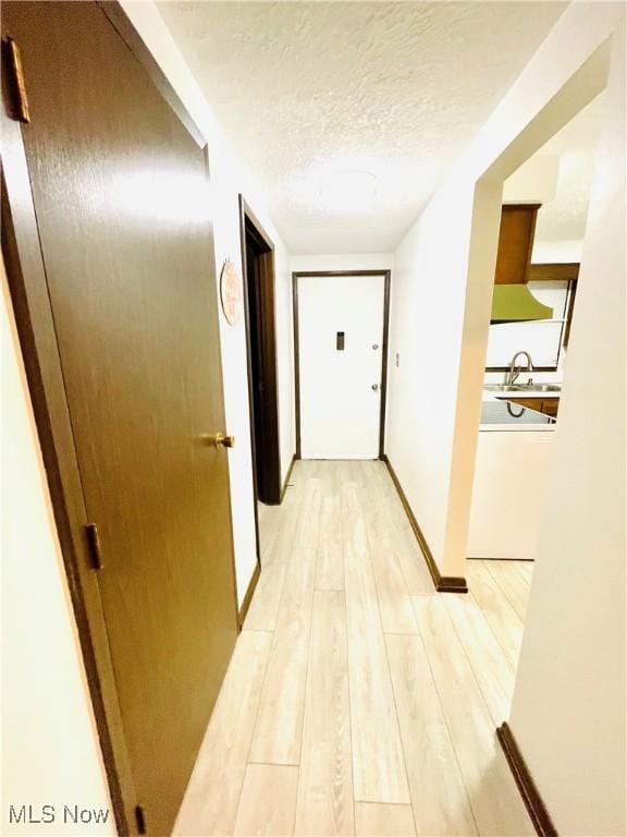 corridor with sink, a textured ceiling, and light wood-type flooring