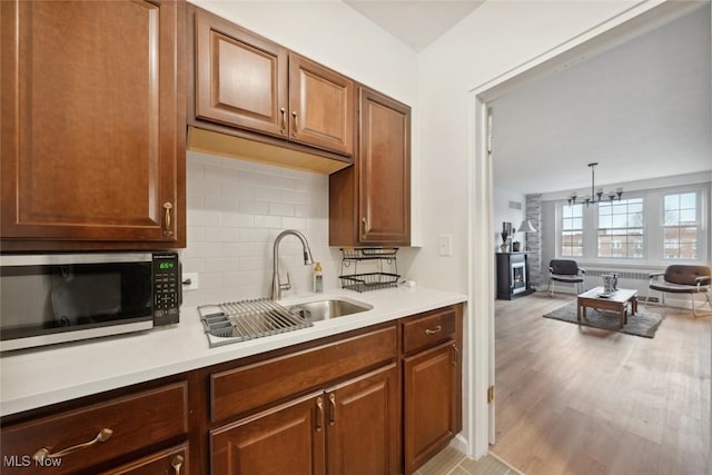 kitchen featuring pendant lighting, sink, decorative backsplash, light hardwood / wood-style floors, and an inviting chandelier