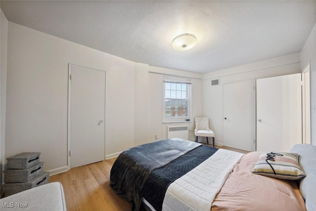 bedroom with radiator heating unit and light hardwood / wood-style flooring