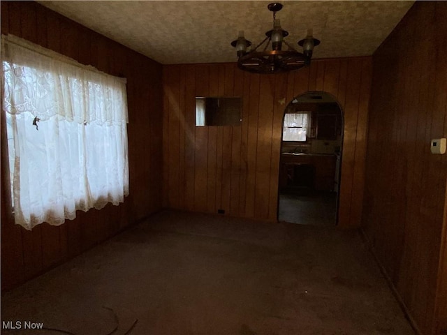 unfurnished dining area with carpet floors, a notable chandelier, and wooden walls