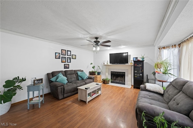 living area with crown molding, a textured ceiling, a tiled fireplace, and wood finished floors