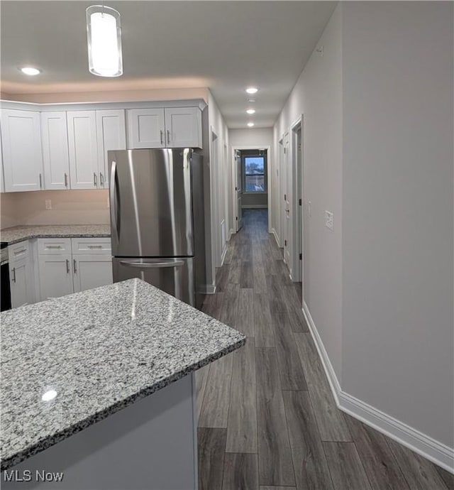 kitchen featuring pendant lighting, white cabinetry, stainless steel fridge, light stone countertops, and dark wood-type flooring