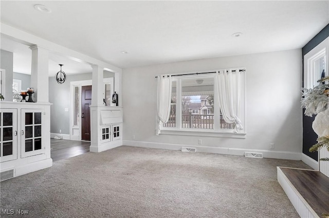 carpeted spare room featuring a notable chandelier and ornate columns